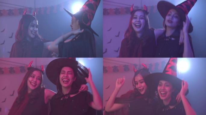 两位穿着万圣节服装的迷人亚洲女士随着音乐跳舞，在五颜六色的紫外线霓虹灯背景下一起玩乐派对。女人享受夜