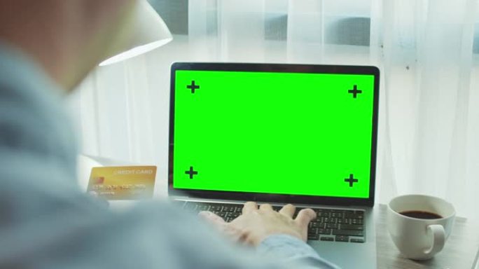 男子使用带有绿屏和手持信用卡的笔记本电脑，特写镜头