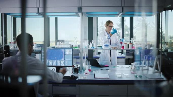穿着白大褂和安全眼镜的女医学家在检查样品时使用微量移液器。高科技实验室的创新，实验药物研究，生物技术