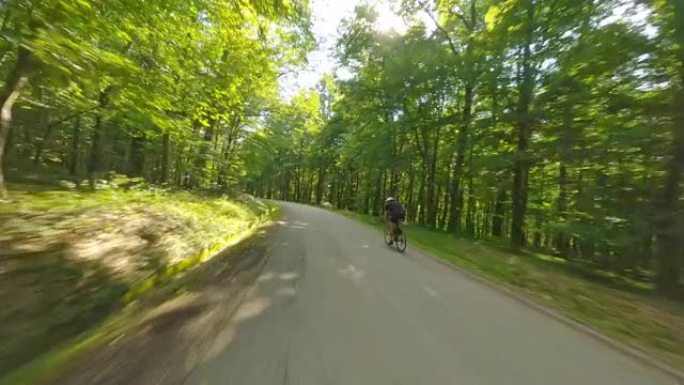 空中成年骑自行车的人在晴天快速驶过森林