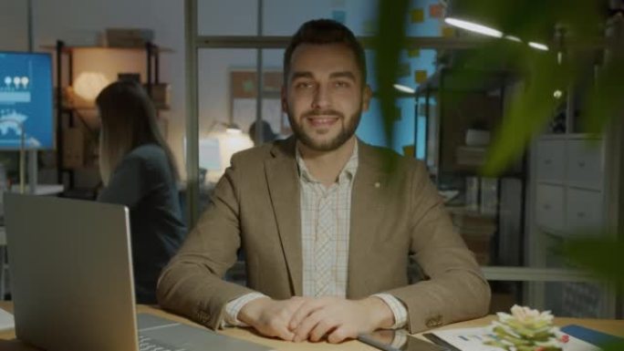 慢动作肖像快乐的年轻企业家晚上坐在办公室微笑