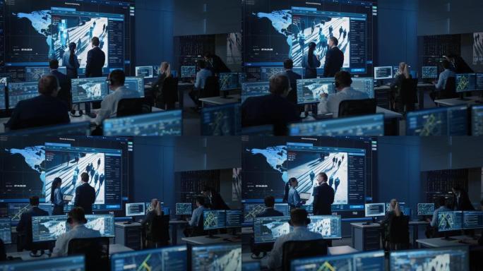 中年男女政府官员在带有带有面部识别软件的卫星监视录像的大数字屏幕旁边讨论工作事项。警方调查人员在工作
