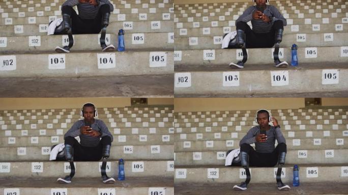 残疾人混合种族男子，假肢坐在体育场上并使用智能手机