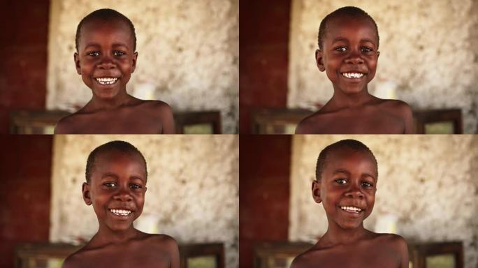 特写镜头，一个顽皮的地道的非洲孩子看着相机，并以模糊的背景强烈地微笑。快乐精力充沛的黑人男孩与世界分