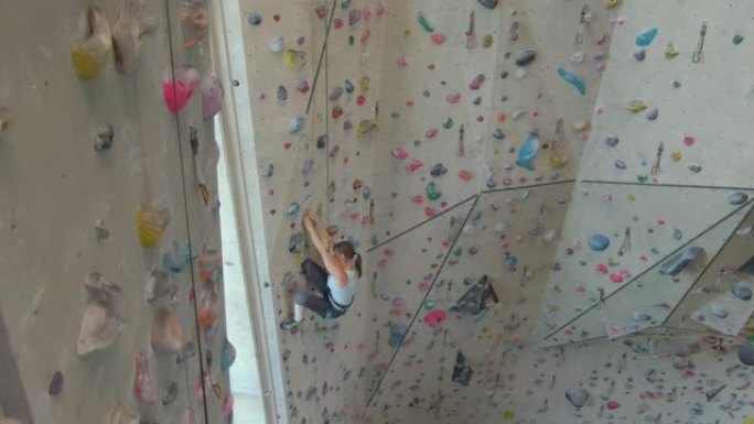 无人机: 健康的年轻女子在室内攀岩中心攀登具有挑战性的路线。