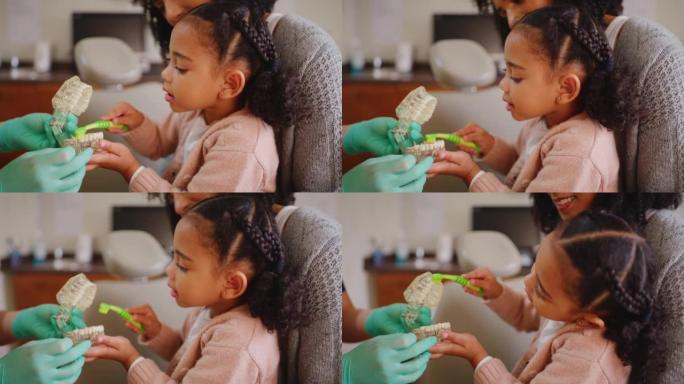 牙医教孩子正确的牙齿卫生习惯。母亲和女儿在牙科预约。小女孩在牙医检查中学习如何在假牙上正确刷牙