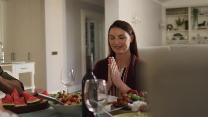 微笑的高加索母亲在家庭用餐前坐在餐桌旁祈祷