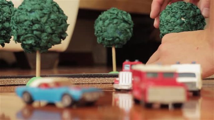 男性的手在家里玩模型火车和微型汽车时捡起一棵玩具树。特写。