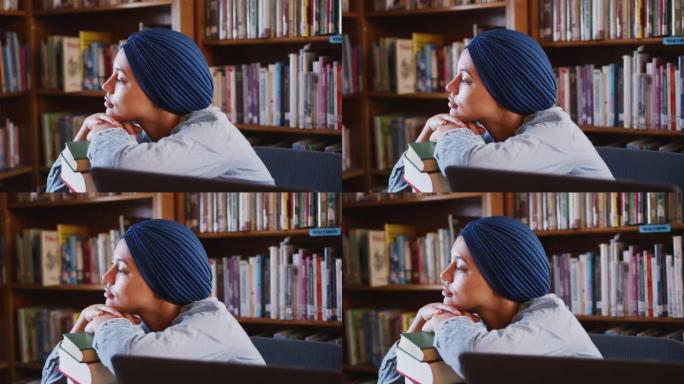 戴蓝色头巾的亚裔女学生坐著靠著一堆书思考