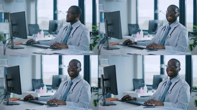 戴眼镜的非裔美国家庭医生正在一家健康诊所的电脑上工作。穿着白色实验室外套的成功黑人医生看着相机，在医