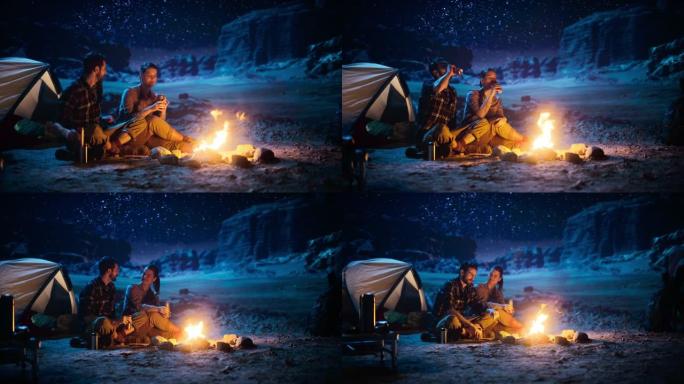 快乐情侣大自然在峡谷露营，坐在篝火旁分享一杯饮料，看夜空。两个旅行的年轻人说话，看看银河系。励志度假