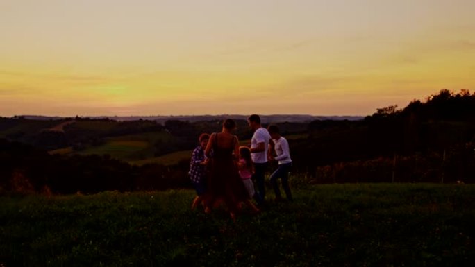 一个年轻家庭的SLO MO剪影，在日落时在草地上的空中跳跃