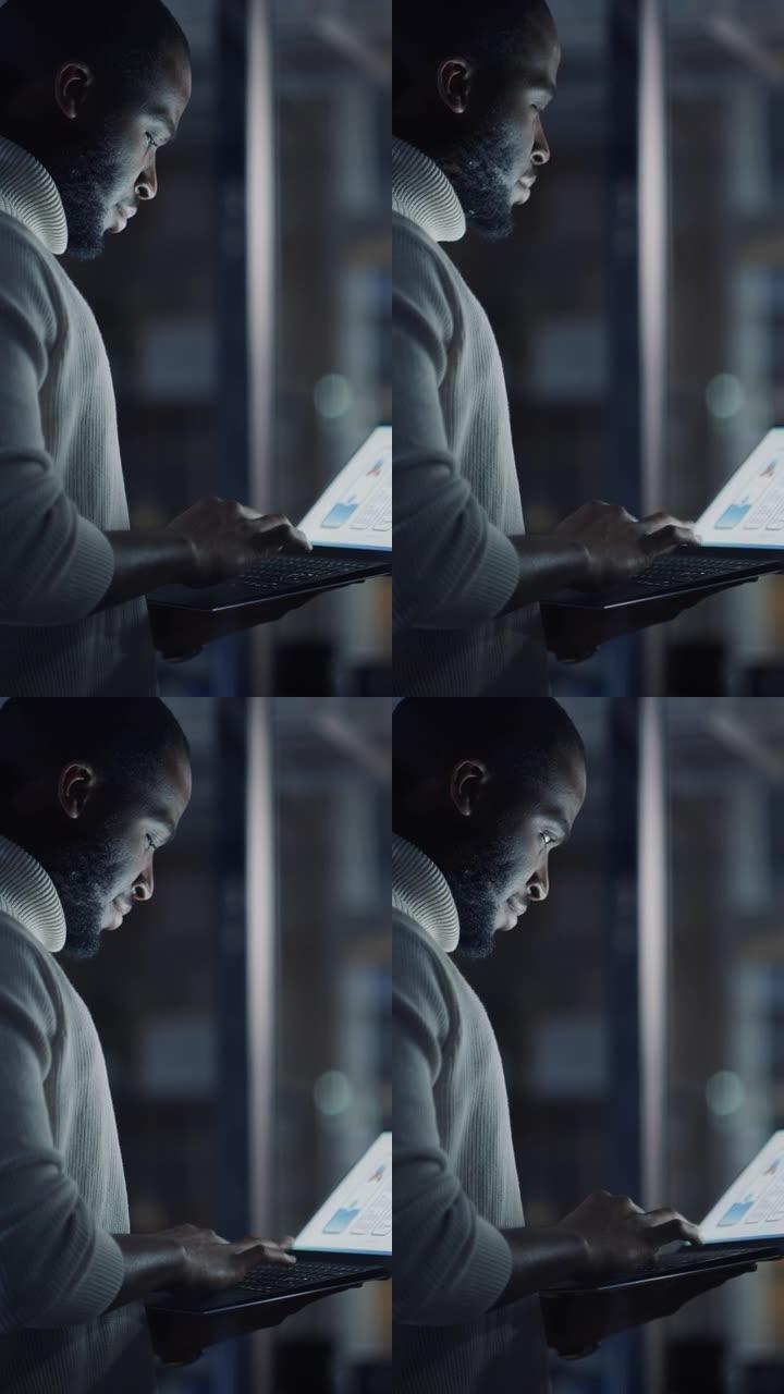 一个英俊的黑人非洲裔美国男性站在一个创意机构的笔记本电脑会议室的垂直肖像。项目经理穿着白色套头衫，致