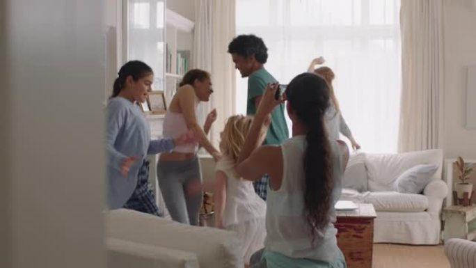 快乐的多民族家庭在家跳舞享受舞蹈庆祝少女使用智能手机在社交媒体上分享激动人心的周末视频