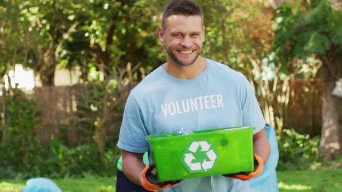 微笑的白人男子穿着志愿者t恤，拿着回收板条箱，收集塑料垃圾