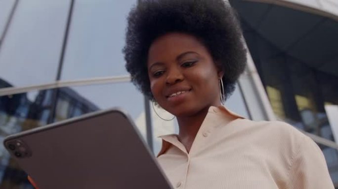 一个年轻的深色皮肤的女商人穿着米色衬衫，使用她的iPad，低角度观看腰部