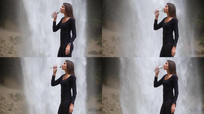 女游客从山上徒步旅行中休息，从瀑布前的水瓶中喝水