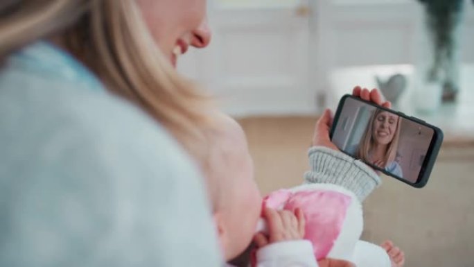 母亲和婴儿使用智能手机与最好的朋友视频聊天在蹒跚学步的快乐妈妈聊天在手机上分享母亲的生活方式