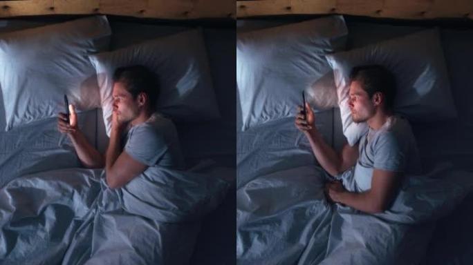 垂直屏幕: 白人男子晚上在家床上使用智能手机。帅哥浏览社交媒体，看新闻，网上购物，晚上和朋友聊天。手