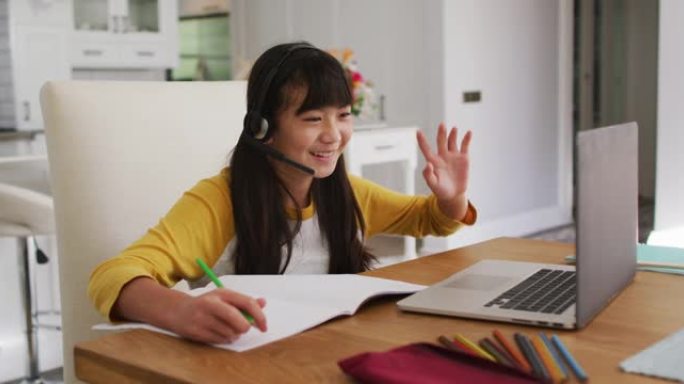 快乐的亚洲女孩在家，坐在办公桌前微笑着在网上学校使用笔记本电脑上课