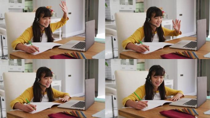 快乐的亚洲女孩在家，坐在办公桌前微笑着在网上学校使用笔记本电脑上课