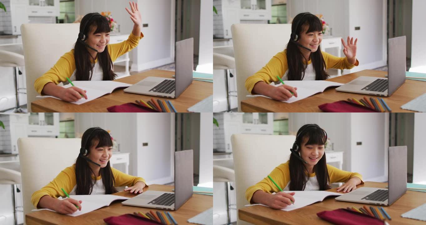 快乐的亚洲女孩在家，坐在办公桌前微笑着在网上学校使用笔记本电脑上课