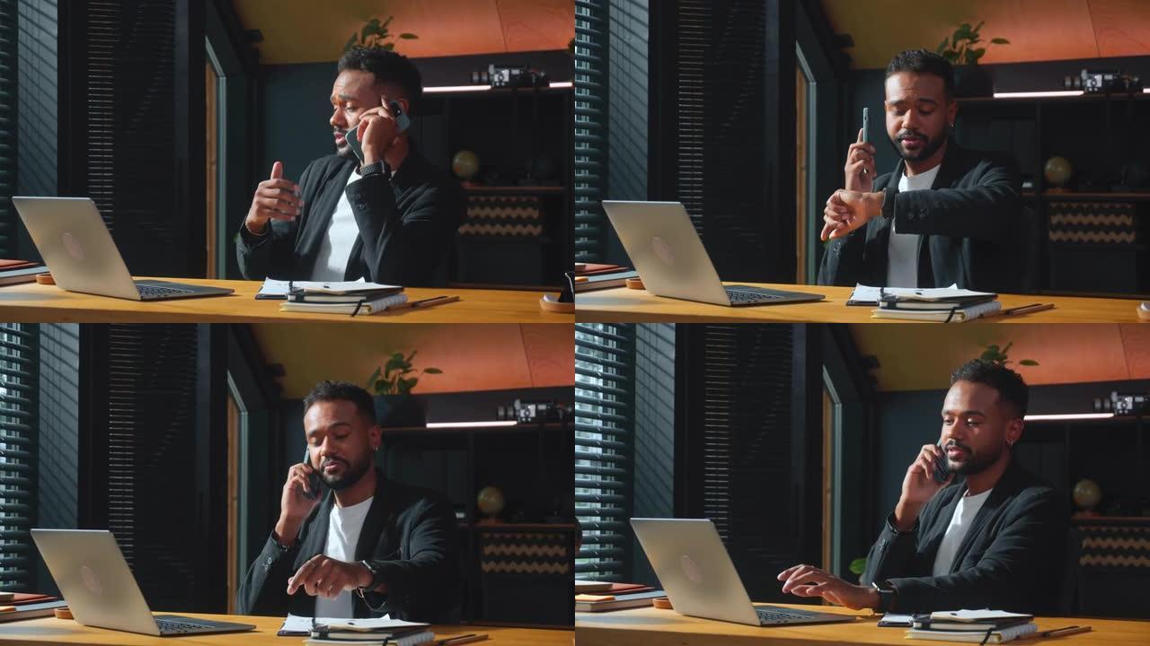 快乐的年轻非洲裔美国商人，执行经理与笔记本电脑合作，在电话检查智能手表上交谈。