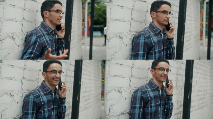 快乐的阿拉伯男子在手机上聊天，在夏日站在城市的户外微笑