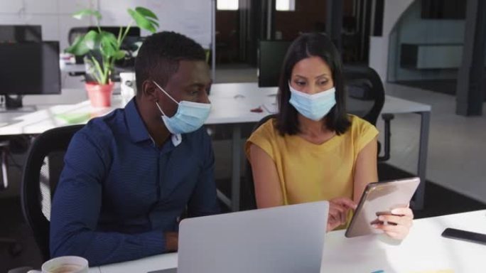 使用平板电脑坐在办公桌前戴着口罩的男女商业同事