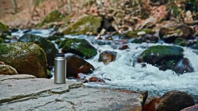 暖水瓶放在流过森林的小溪旁的岩石上