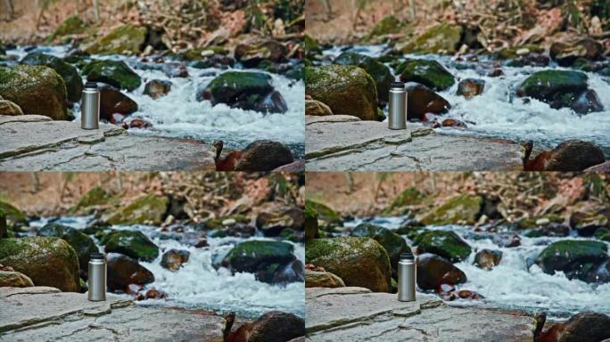 暖水瓶放在流过森林的小溪旁的岩石上