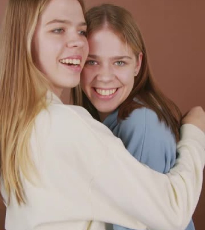 幸福的双胞胎女孩拥抱和微笑的垂直肖像