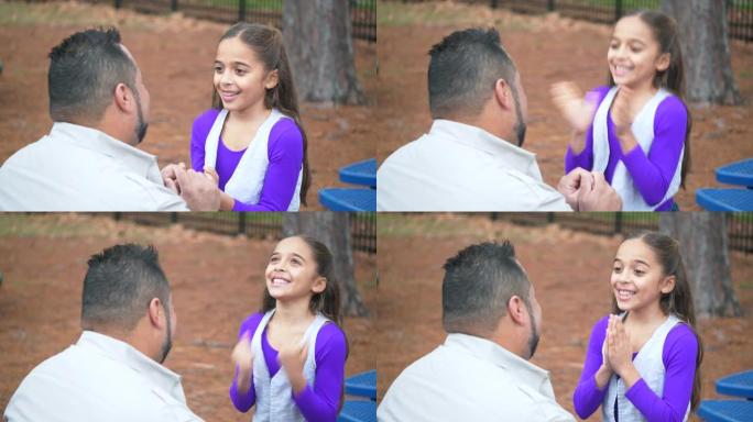 西班牙裔女孩从公园的父亲那里得到了喜讯，拥抱