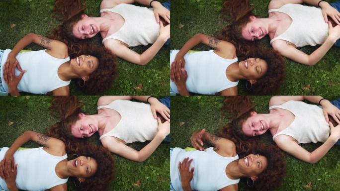 从高处看:两个多民族妇女躺在公园草坪上，有说有笑。不同的女性青少年享受彼此的陪伴，一起在外面度过时光