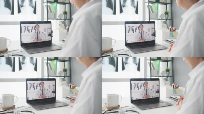 年轻的亚洲女士医生在白色医疗制服使用笔记本电脑通话视频电话与高级医生在医疗诊所或医院的办公桌。