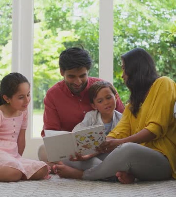 在家微笑的家庭坐在休息室的地板上一起看书的垂直视频