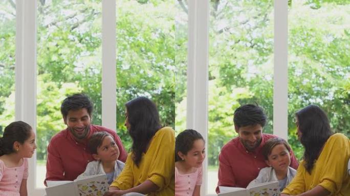 在家微笑的家庭坐在休息室的地板上一起看书的垂直视频