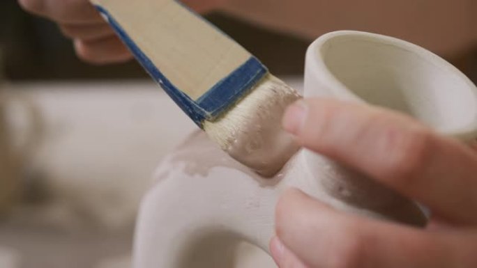 在陶艺工作室用釉刷在锅上绘画的女陶工的特写视图