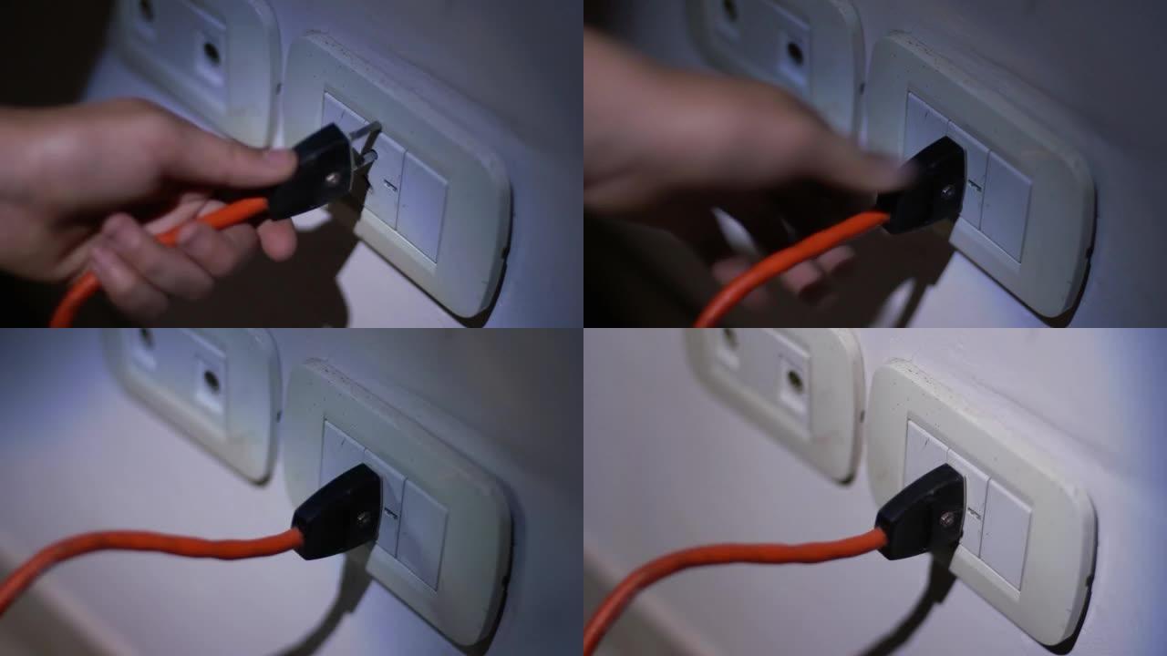 在停电或停电期间，在黑暗中使用手电筒在公寓墙壁上连接插座的男性手。特写。