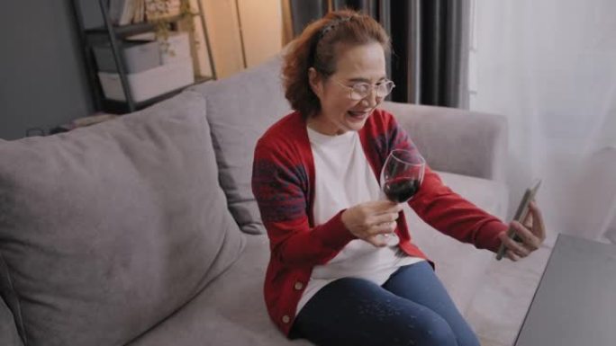 微笑的退休老妇人拿着酒杯敬酒网上约会与男友通过视频通话。