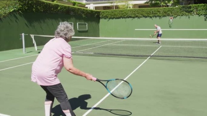 高加索高级夫妇在阳光下的室外球场上打网球