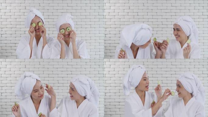 肖像亚洲两个年轻的女人在眼睛上做黄瓜面部护肤面膜，同时在家里一起笑放松，微笑的女孩朋友玩得开心。虚拟