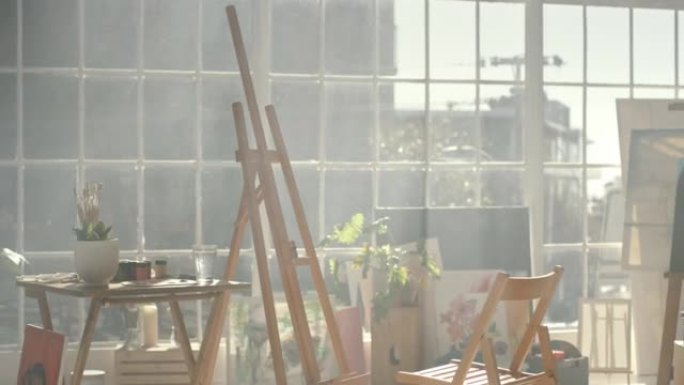 一个空的艺术工作室，房间里有一个画架和椅子。在温暖的日子里，城市的画家公寓里阳光照耀着家具，帆布，刷
