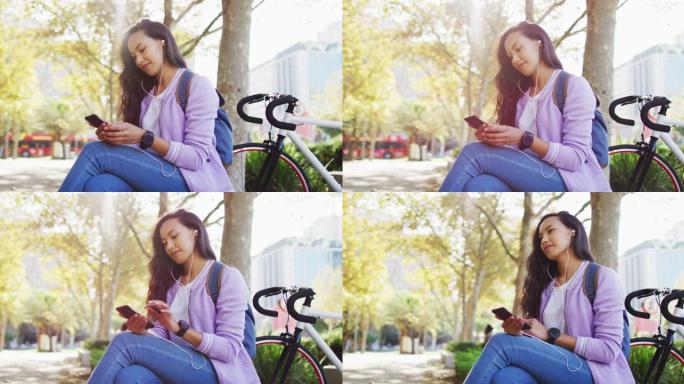坐在公园里使用智能手机戴着耳机的亚洲妇女