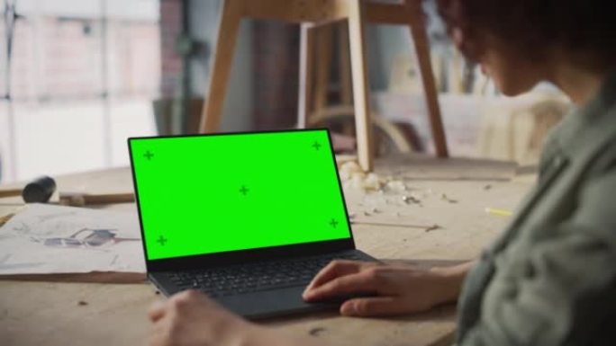 在带有绿屏模拟显示的笔记本电脑上工作的家具设计师的肩膀上。创意女性为木工项目准备设计。