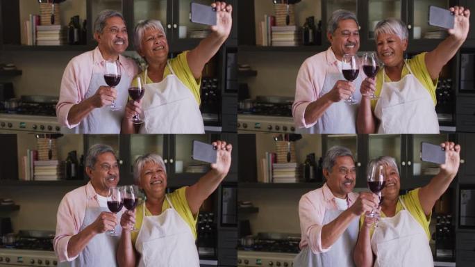 快乐的高级混血夫妇在厨房里用葡萄酒自拍照敬酒
