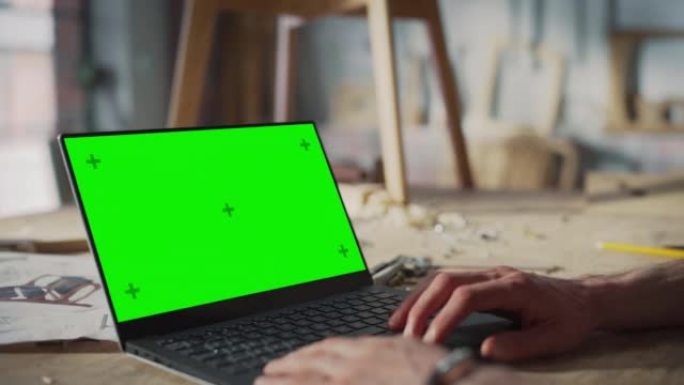 使用带有绿屏色度键显示的笔记本电脑的人的特写镜头。在木工工作室车间工作的有创造力的人。