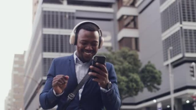 跳舞的商人在城市里用无线耳机在手机上听音乐。微笑、快乐和专业的男性庆祝获得晋升。浏览技术的开朗家伙。