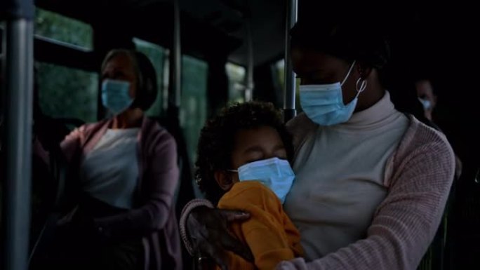 非裔美国妇女在公共汽车上戴着covid面具的睡着的男孩