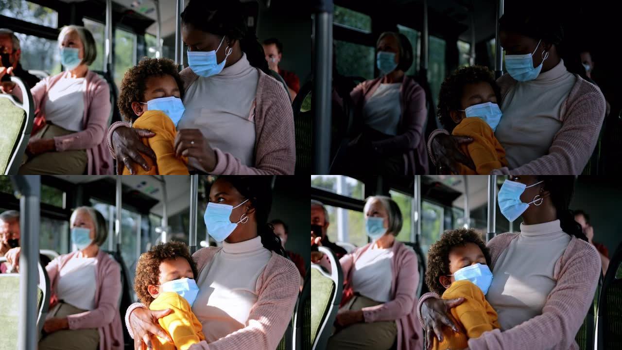 非裔美国妇女在公共汽车上戴着covid面具的睡着的男孩